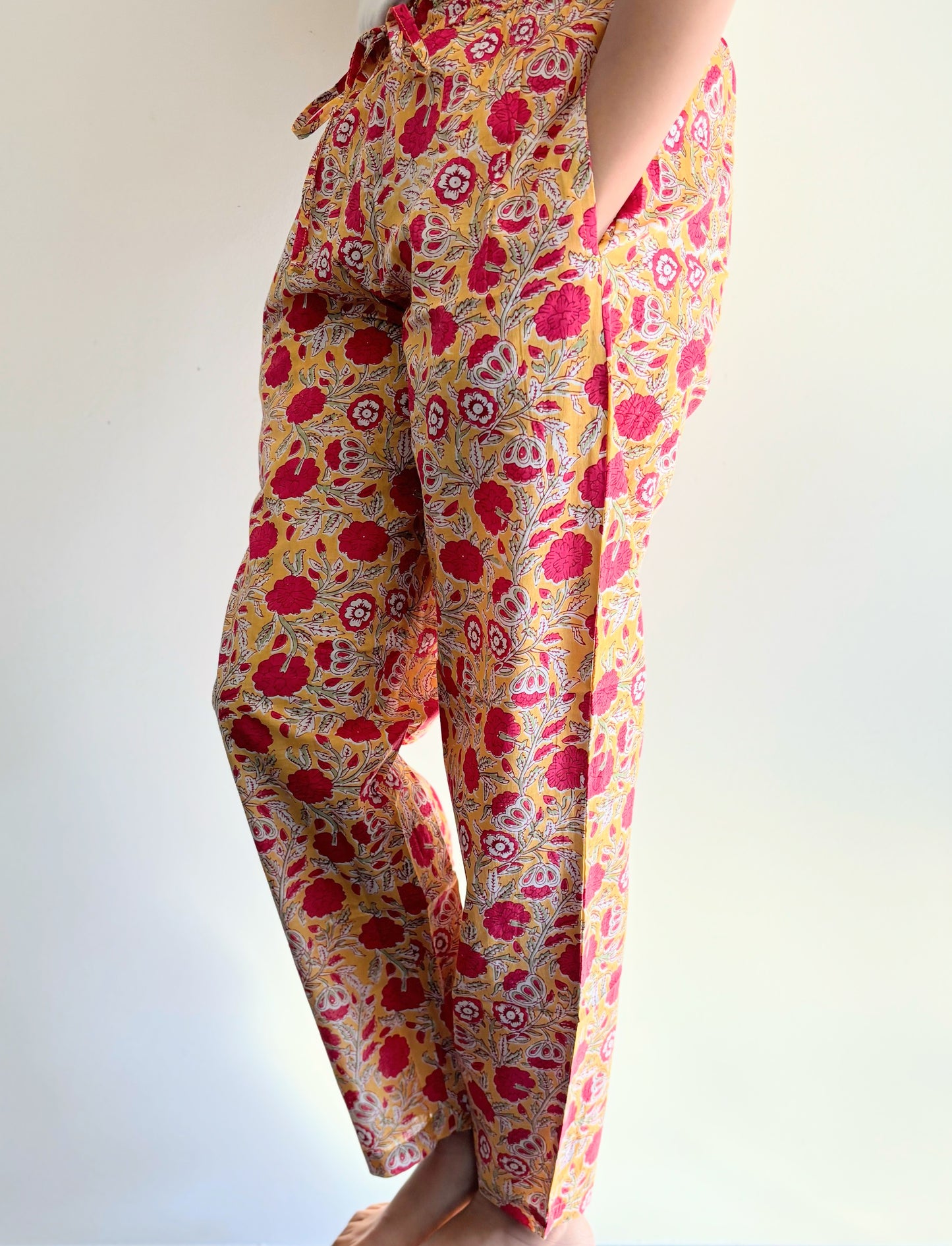 Set of two cotton pajama pants for women, with one pair in a yellow print with red flowers and the other in navy blue with orange flowers, both with pockets and elastic waistbands.