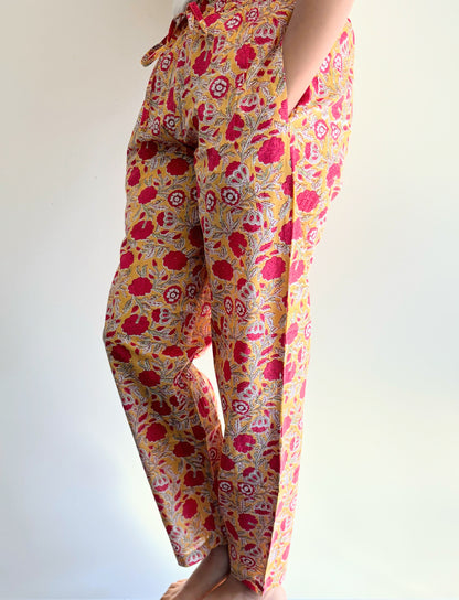 Set of two cotton pajama pants for women, with one pair in a yellow print with red flowers and the other in navy blue with orange flowers, both with pockets and elastic waistbands.