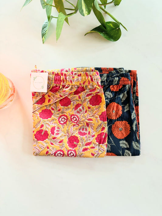 Two-pack of women’s 100% cotton pajama pants: one pair with red flowers on a yellow background, and the other with orange flowers on a navy blue background, both with pockets and elastic waist.