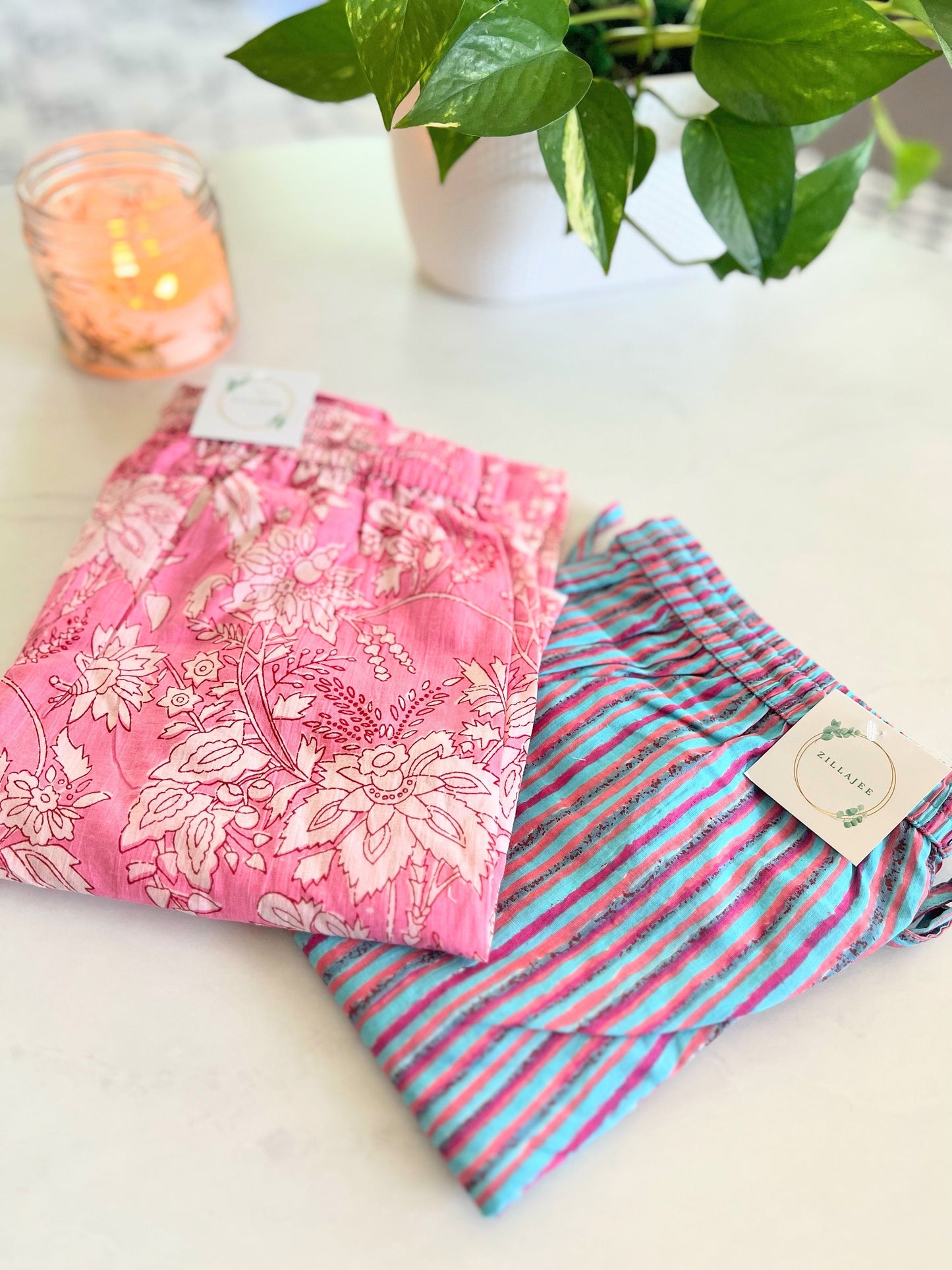 Two-pack of 100% cotton pajama pants for women: one pair featuring white flowers on a pink background, and the other with pink and blue stripes, both with pockets and an elastic waist for comfort.