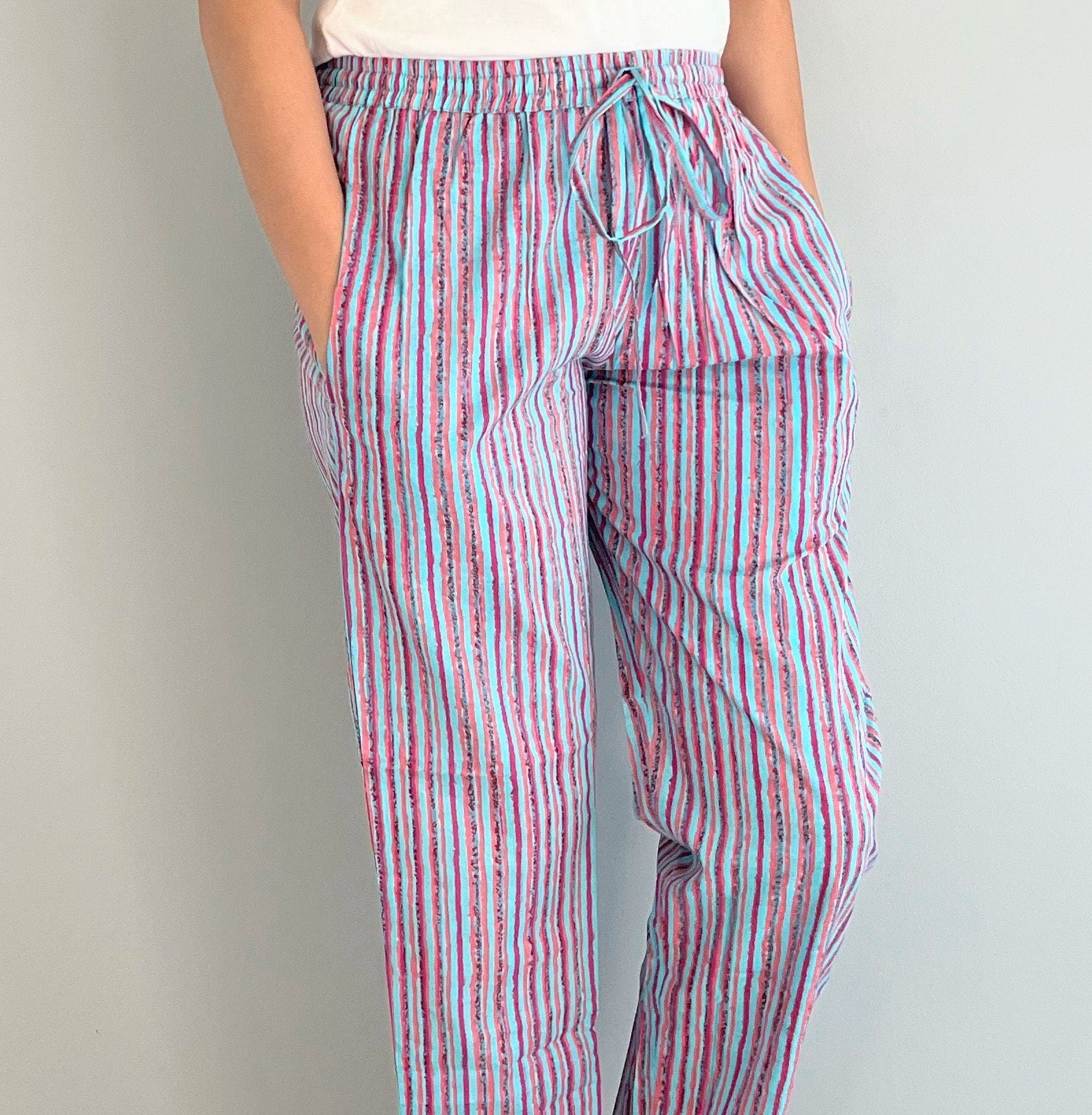 Relaxing 2-pack pajama pants for women in 100% cotton: one pair with white flowers on a pink background, and the other with a playful pink and blue striped pattern, both with elastic waist and side pockets.